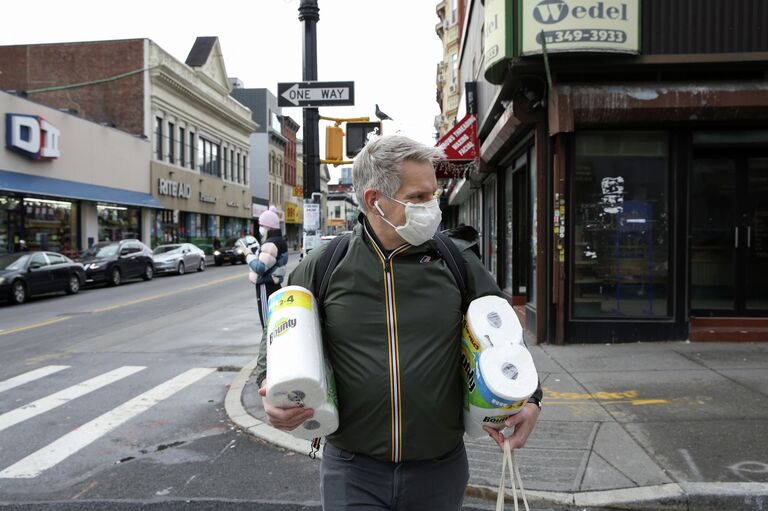 Мужчина идет из магазина в защитной маске во время вспышки COVID-19, Нью-Йорк