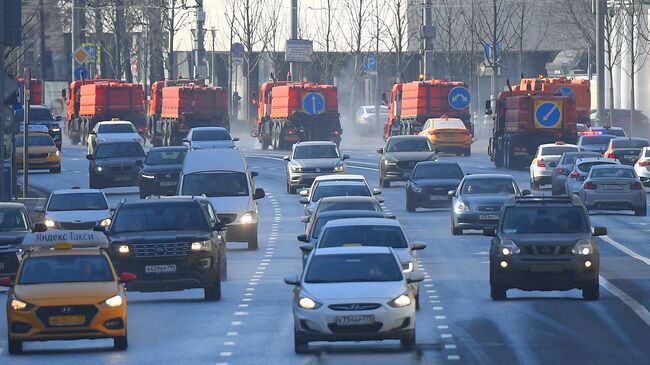 На дальнем плане - автомобили коммунальной службы производят мытье асфальтового покрытия с использованием специального моющего средства в Москве