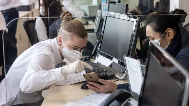Сотрудница в защитной маске ведет прием посетителей в одном из отделений банка Открытие