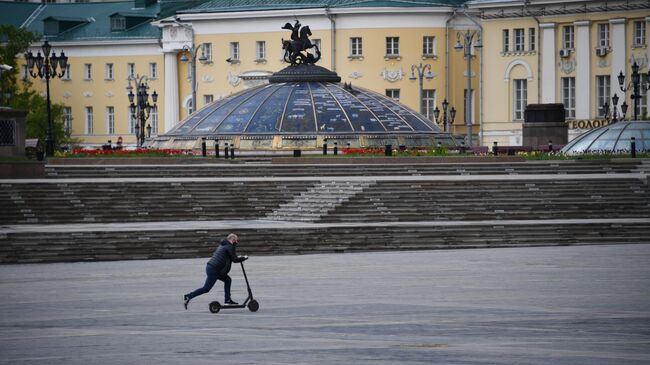 Мужчина едет на электросамокате по Манежной площади в Москве