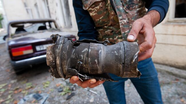 Мужчина держит в руках осколок от разорвавшегося снаряда в результате обстрела на одной из улиц города Мартуни