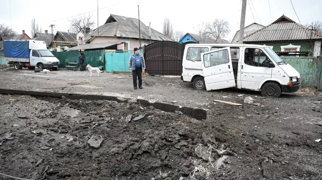 Воронка от взрыва и поврежденный в результате обстрела автомобиль в Киевском районе Донецка