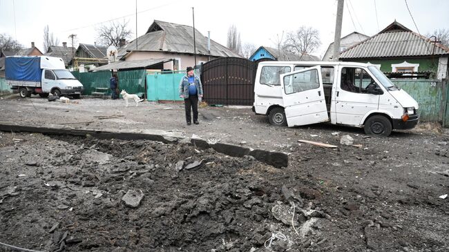 Воронка от взрыва и поврежденный в результате обстрела автомобиль в Киевском районе Донецка