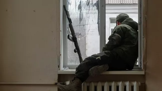 Военнослужащий ДНР сидит у окна во время боестолкновений в Левобережном районе Мариуполя