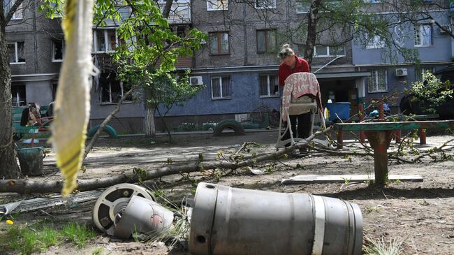 Жительница стирает одежду во дворе разрушенного дома в Левобережном районе Мариуполя