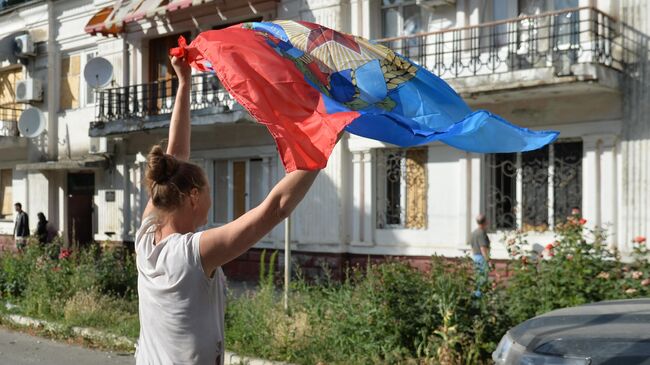 Местная жительница с флагом ЛНР, подаренным бойцами 6-го казачего полка имени Платова ЛНР и специального полка полиции имени Героя России Ахмата-Хаджи Кадырова у здания администрации в Лисичанске