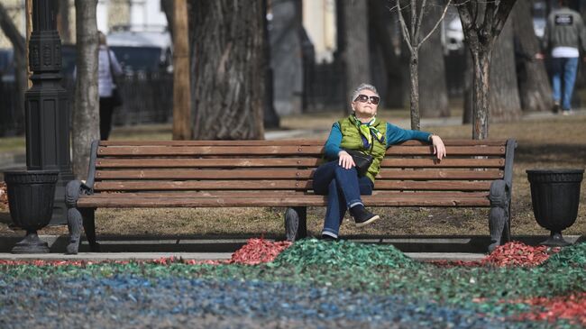 Женщина отдыхает на скамейке во время теплой погоды в одном из парков Москвы