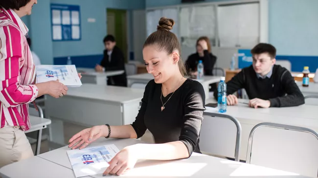Преподаватель раздает пакеты с экзаменационными заданиями перед началом единого государственного экзамена по географии