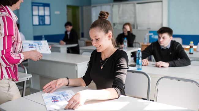 Преподаватель раздает пакеты с экзаменационными заданиями перед началом единого государственного экзамена по географии