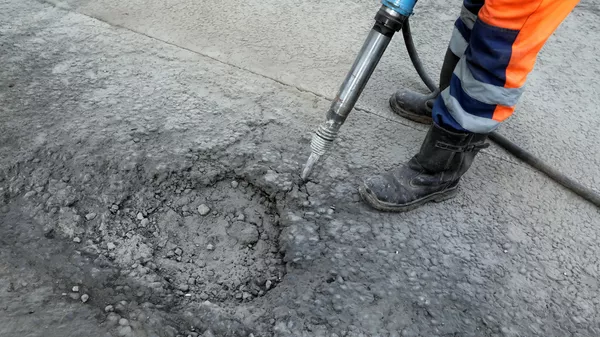 Рабочий бригады ГБУ Автомобильные дороги демонтирует старое дорожное полотно пневматическим отбойным молотком в Москве
