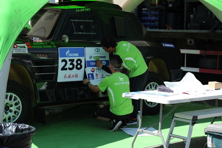 Китайские гонщики наклеивают опознавательные наклейки, ралли Шелковый путь-2019