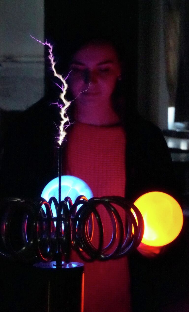 Сотрудница демонстрирует имитацию грозового поля с помощью генератора тока и плазменных шаров